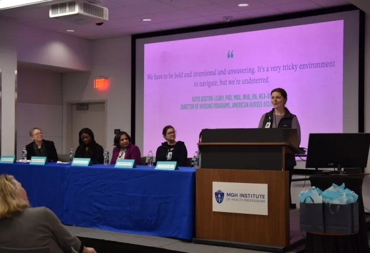 A woman stands at a podium while a panel of people watches her