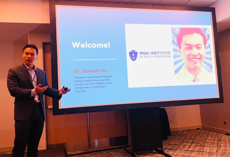 A man stands in front of a screen with his photo and the word Welcome on it. 