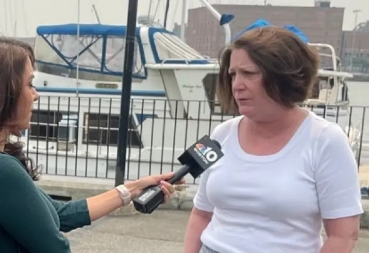 A women on the left holds a microphone with a camera behind her while another women speaks into the microphone