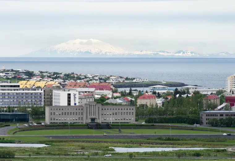 a green lawn with buildings in the background and a mountain in the distance across a body of water