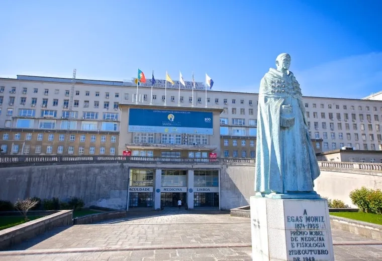 large concrete building with many windows, 6 flags on top and statue in the front