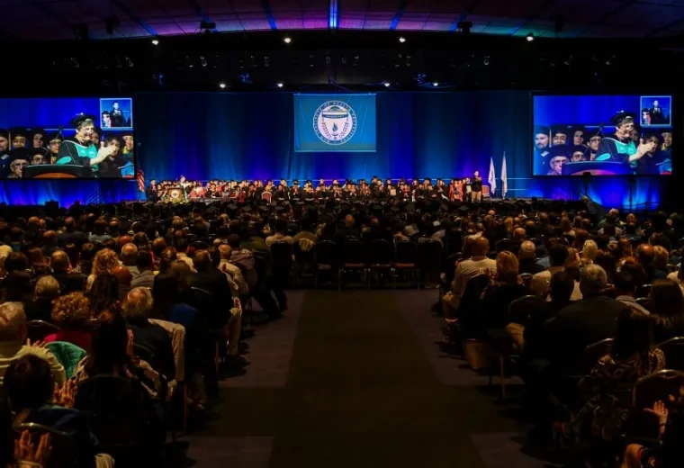An audience sits in front of a stage while people wearing academic robes sits on the stage