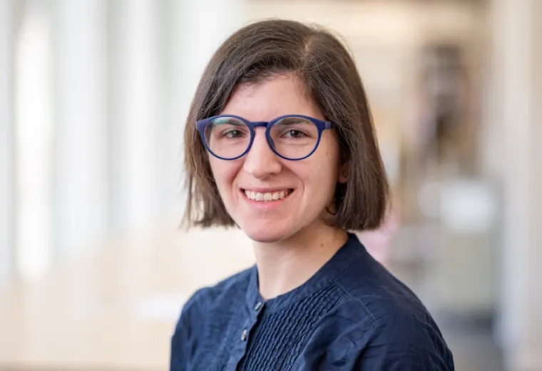 Emily Rosen has short, straight, brown hair, is wearing blue glasses, and is wearing a dark blue blouse.