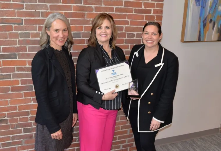 Three women pose with the one in the middle holding an award
