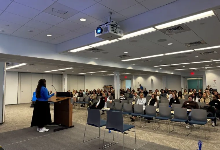 Woman standing on stage speaking to large audience in chairs
