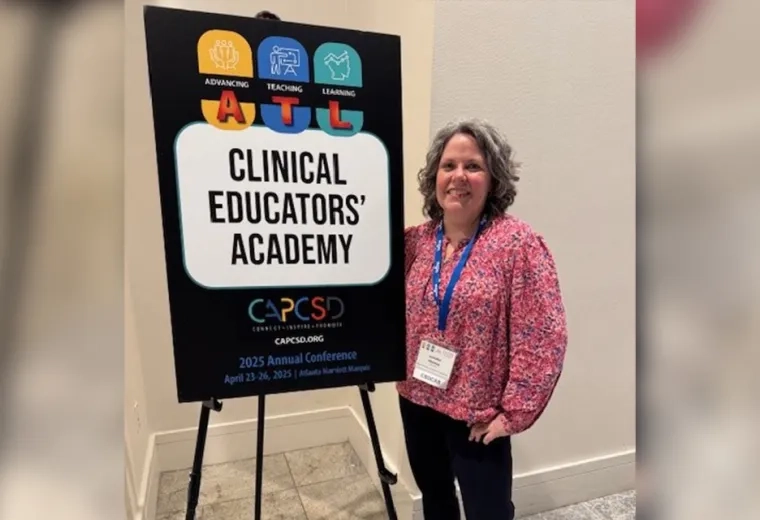 A woman stands in front of a sign that says Clinical Educators' Academy