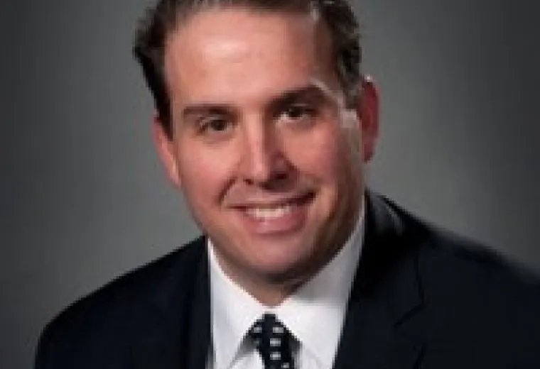 Michael Cassara has short brown hair and is wearing a black suit, with a white shirt, and black and white tie.