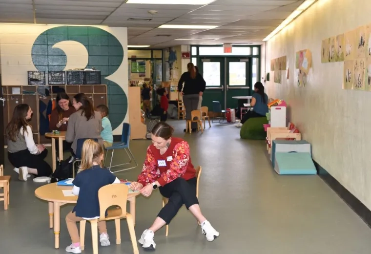 A woman sits at a small table with a child while people in the background do the same