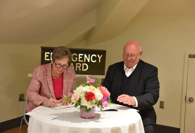 Two people sit next to each other at a table writing on paper