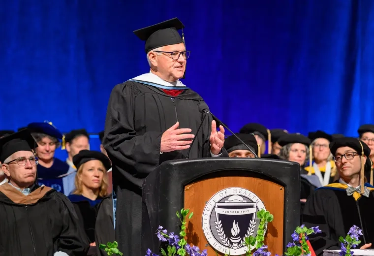 A man wearing a graduation robe stands at a podium