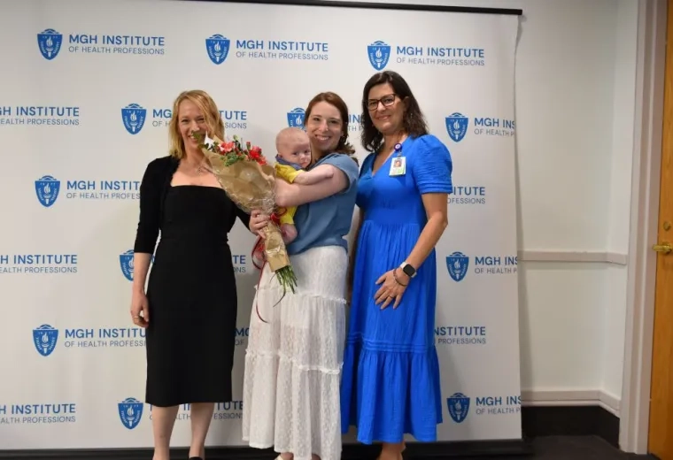 Three people stand in front of a backdrop with one of them holding a baby