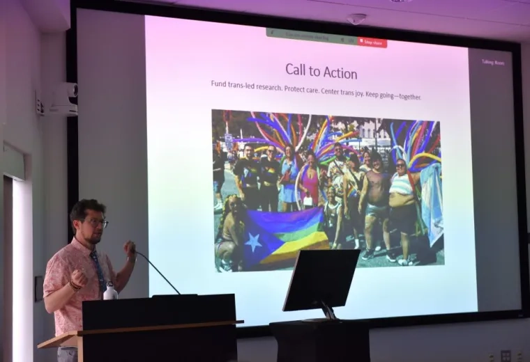 Man standing to left of screen with group photo on it
