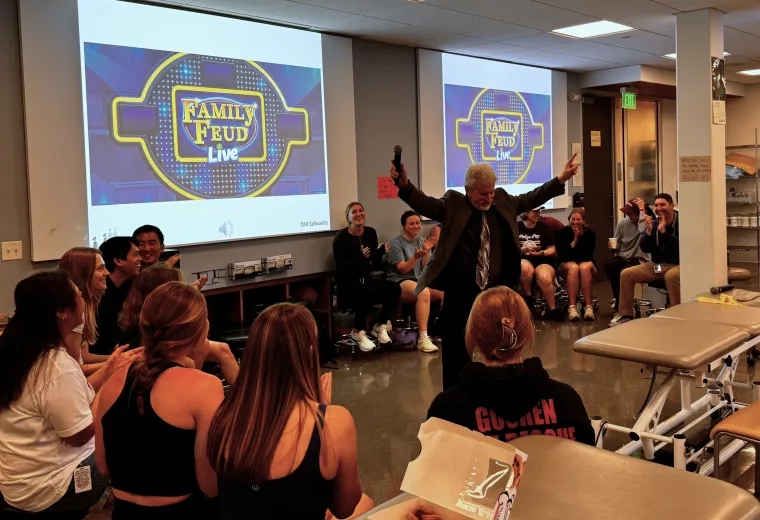 Professor with arms raised in front of family feud screens