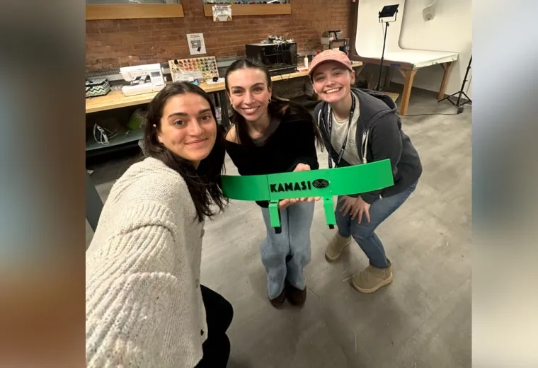 Three women pose holding up a green device