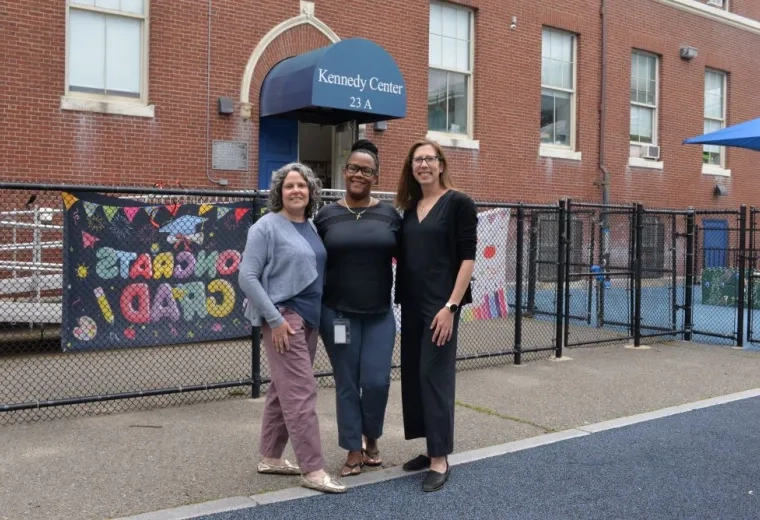 Three women pose outside a building that has a sign that reads Kennedy Center