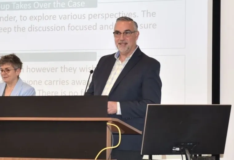 A man stands at a podium with a woman standing next to him and empty seats to his right