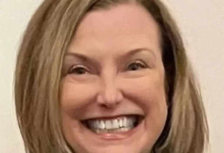 Woman with blonde hair smiling and wearing a green shirt and scarf