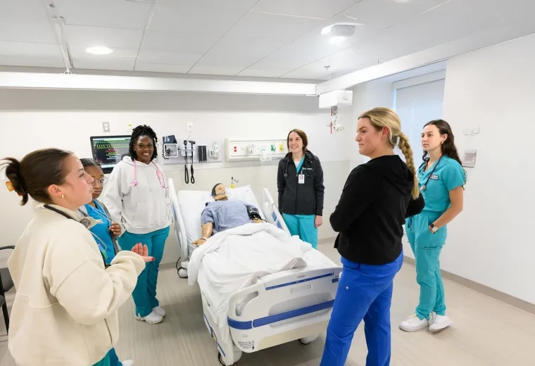 women in scrubs around a manikin in a hospital bed
