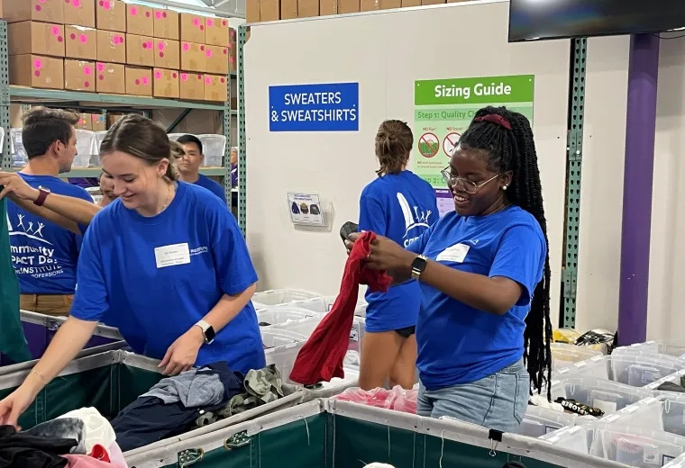 women and men in matching blue t shirts printed with "community impact" sort clothes into bins