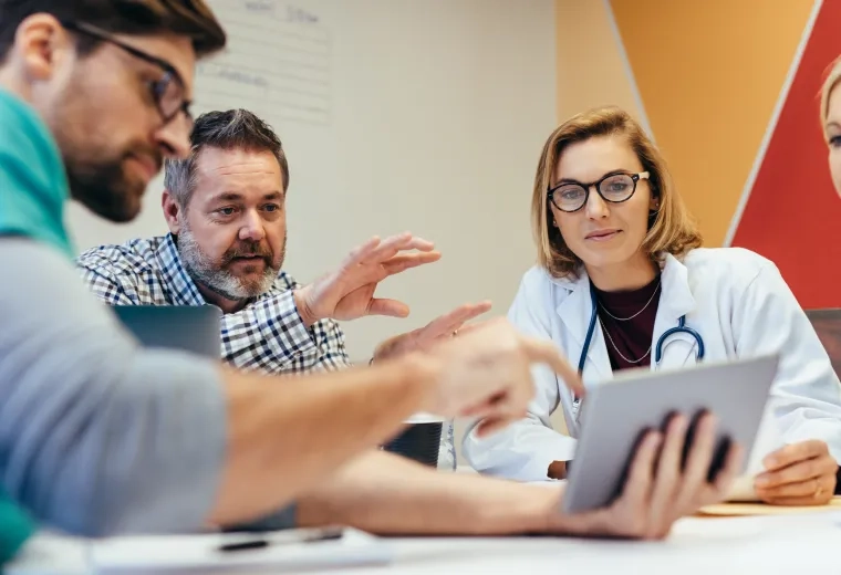 meeting where a bearded man in a business shirt points out something on an ipad to a woman in a lab coat