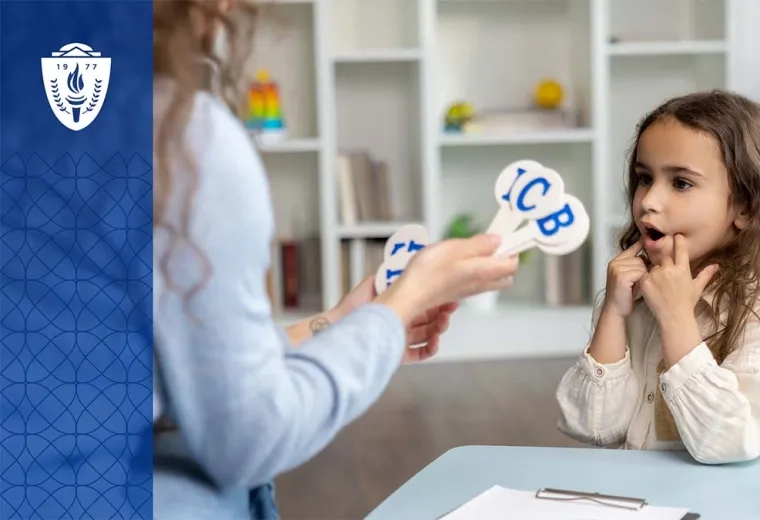 Young girl sitting at desk looking at a teacher holding sticks with alphabet letters on them
