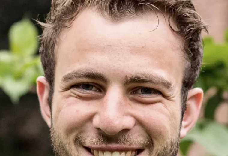 Man with short brown hair wearing a purple shirt smiling and looking at camera