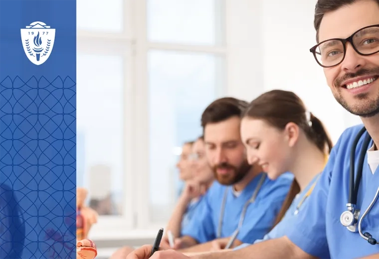 Group of physician assistants wearing stethoscopes and blue scrubs sitting at table