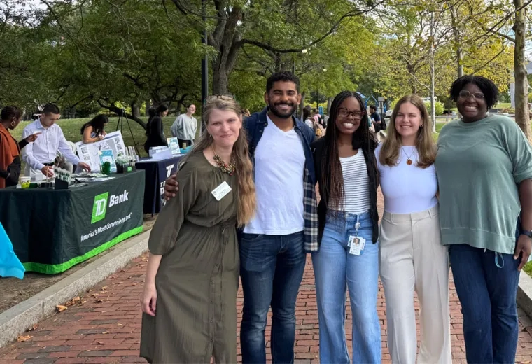 5 people standing on a brick path in front of trees huddles together