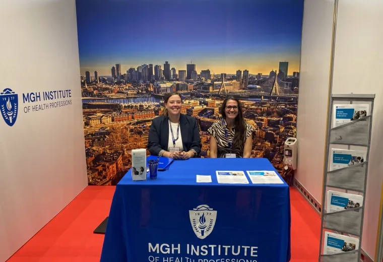 two women sitting at MGH Institute booth with a background of Boston