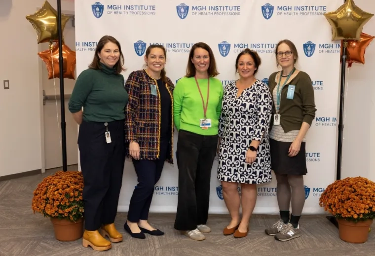Five women stand against a backdrop posing for a photo