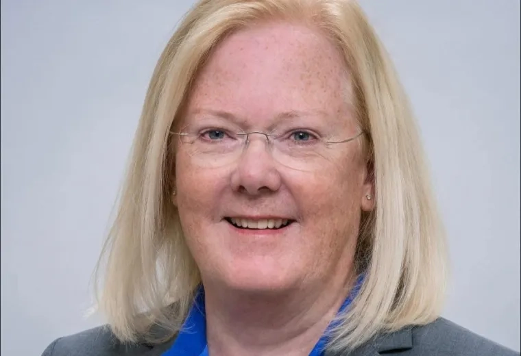 Headshot of woman with blonde hair wearing a gray jacket in front of a solid light gray background