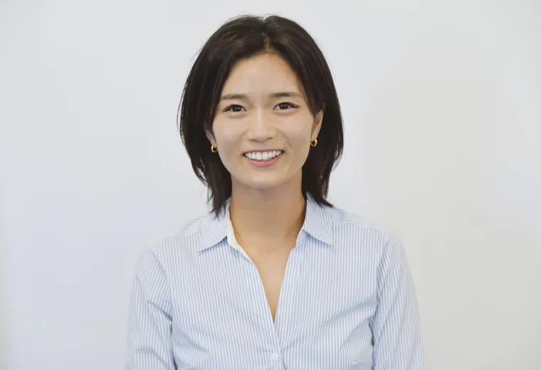 Headshot of woman with black hair standing against a solid white background wearing a blue collared shirt