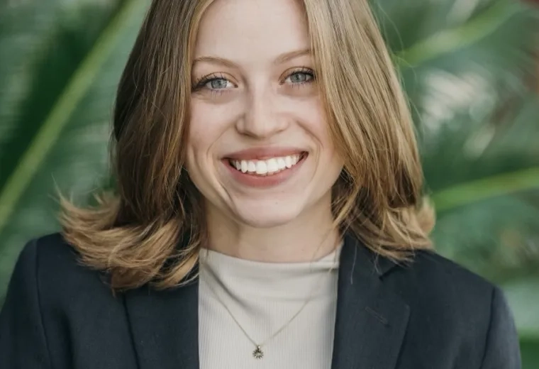 Headshot of woman with blonde hair wearing a tan shirt and black jacket