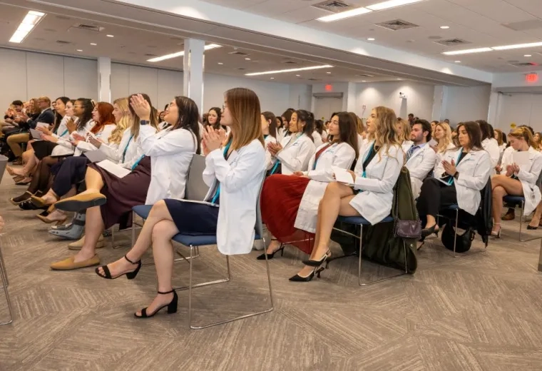 An audience of people in white coats sits in rows