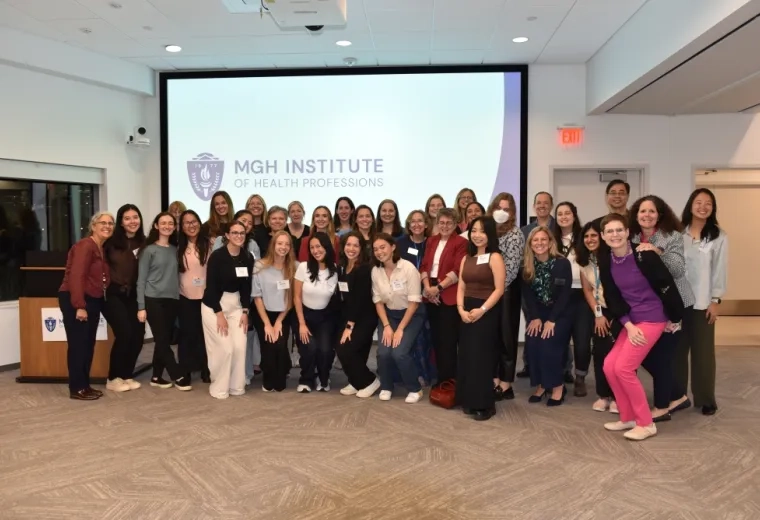 A large group of people stand together for a photograph in front of a screen that says MGH Institute of Health Professions