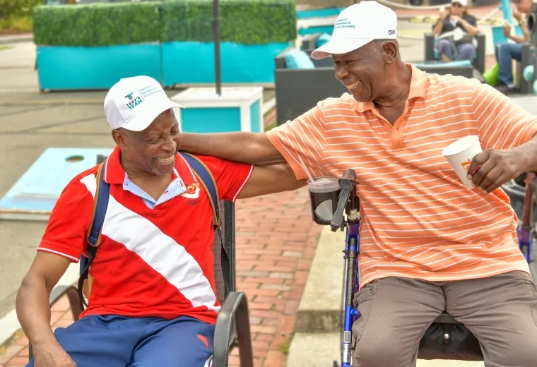 Two men sit outdoors smiling with their arms around their shoulders