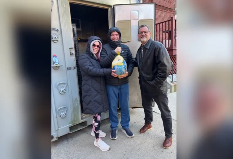 three people in front of a large walk in freezer hold a wrapped turkey
