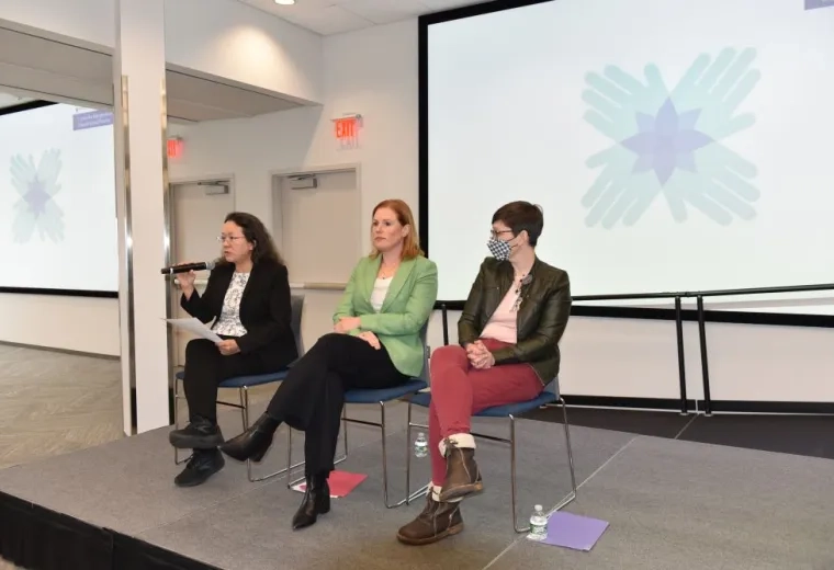 3 women sitting in chairs on a stage in front of a screen 