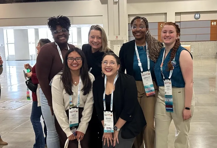Five women pose in a convention center wearing lanyards