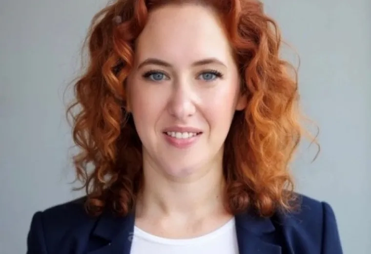 Headshot of Woman with wavy red hair wearing a white shirt and a blue jacket
