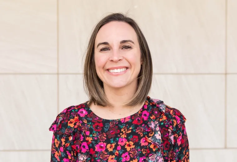 Headshot of woman with shoulder length brown hair smiling at camera and wearing floral shirt
