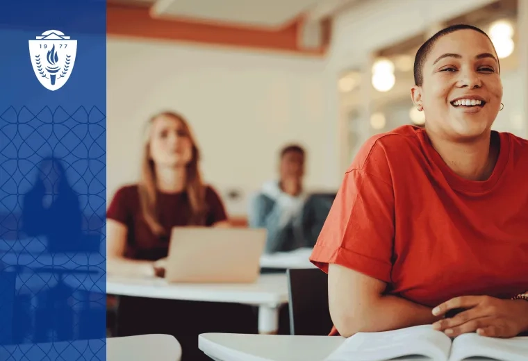 Woman wearing a red shirt sitting a desk in a classroom with a textbook open on the desk