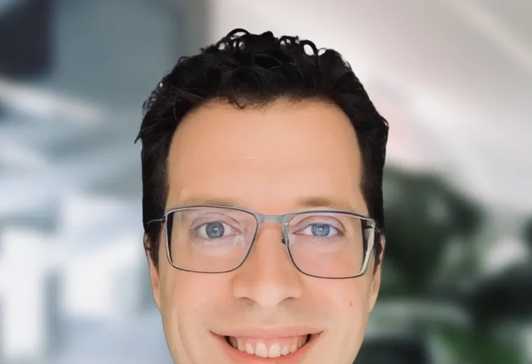 Headshot of man with short black hair wearing glasses and a gray polo shirt in front of a blurred background