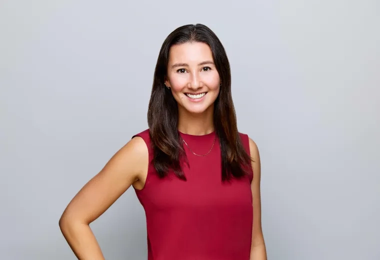 Headshot of woman with long dark hair wearing a red shirt against a gray background.