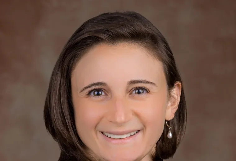Headshot of woman wearing white shirt and black jacket against a brown backgroud