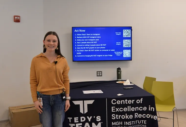 A woman stands in front of a table and screen 