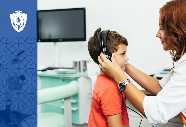 Woman wearing a lab coat putting headphone on a young boy wearing an orange T-shirt