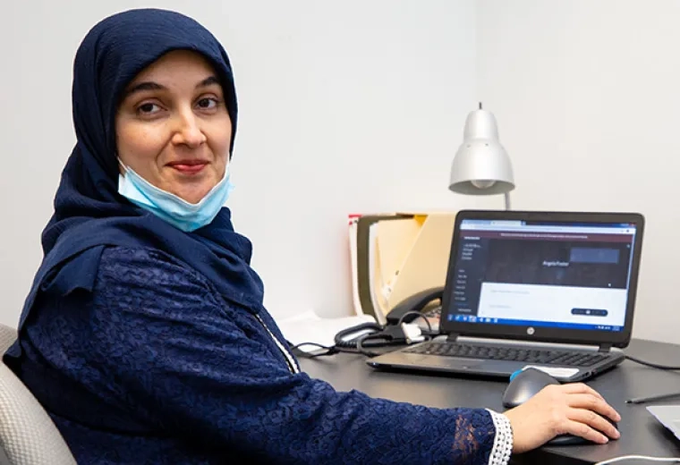 A woman sits at a desk with a laptop computer in front of her