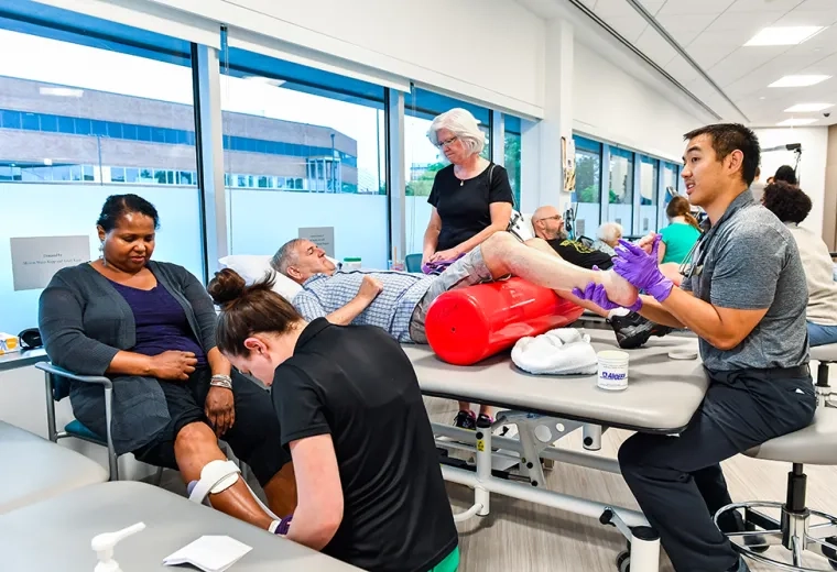 Patients sit on chairs or lie on a table while medical professionals interact with their limbs