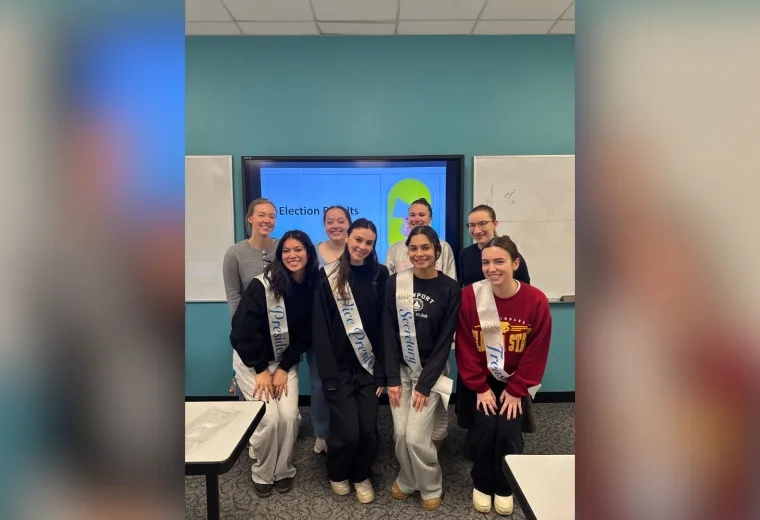 8 women standing in front of a screen with sashes on 